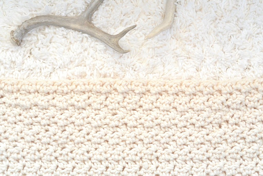 creamy white crochet blanket on a white rug with antlers