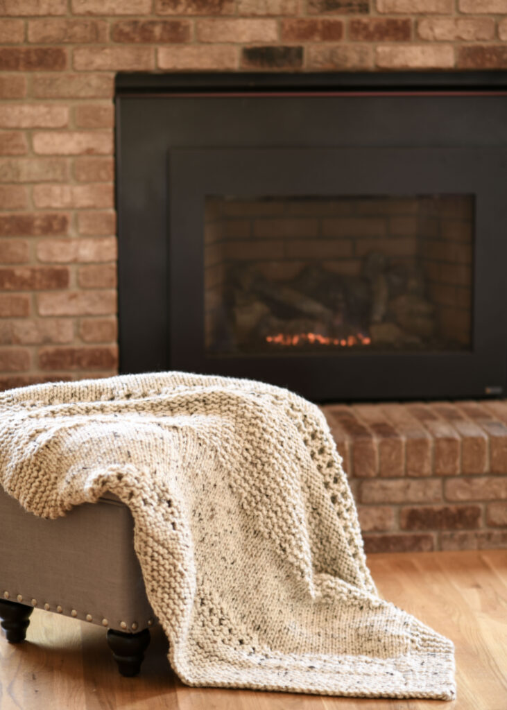 an oatmeal colored chunky knit blanket laid across an ottoman